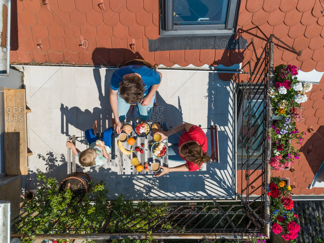 Aerial view of family having breakfast on rooftop balcony in morning sun in Spring.