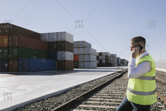Man on railway tracks in front of cargo containers talking on cell phone