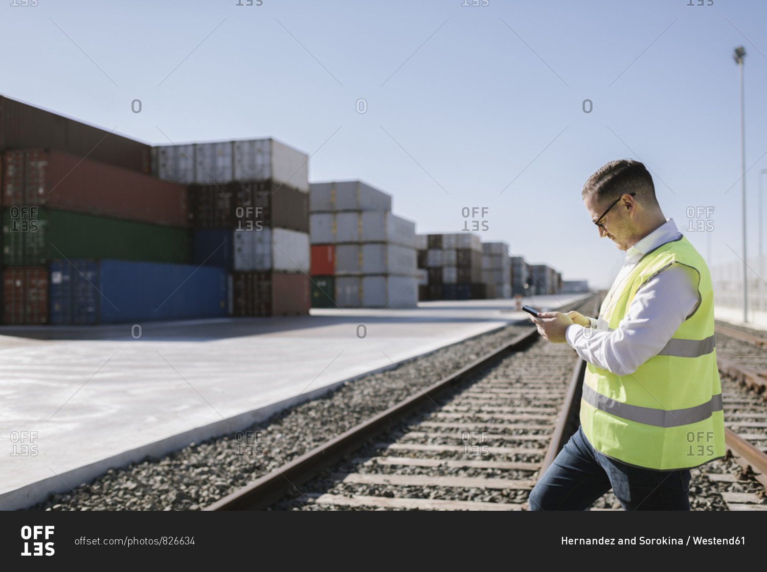 Man on railway tracks in front of cargo containers using cell phone