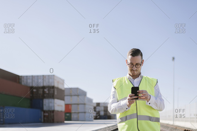 Man on railway tracks in front of cargo containers using cell phone