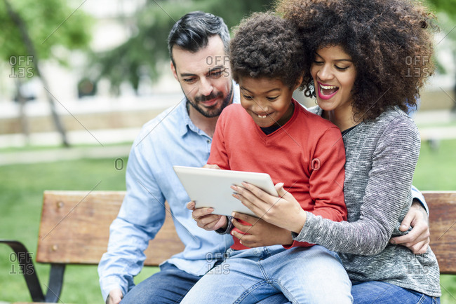Family sitting on a park bench- using digital tablet