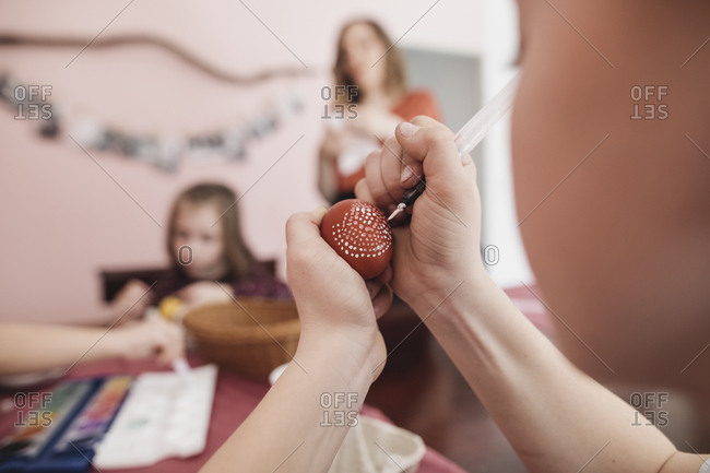 Girl painting Easter egg at home with family in background