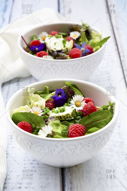 Two bowls of leaf salad with raspberries and cream cheese garnished with edible flowers