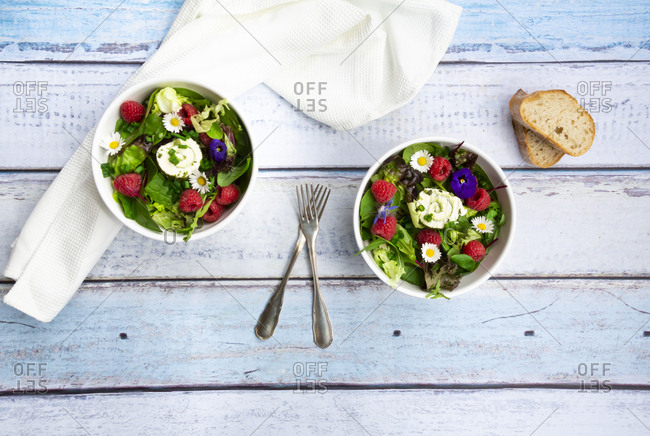 Two bowls of leaf salad with raspberries and cream cheese garnished with edible flowers