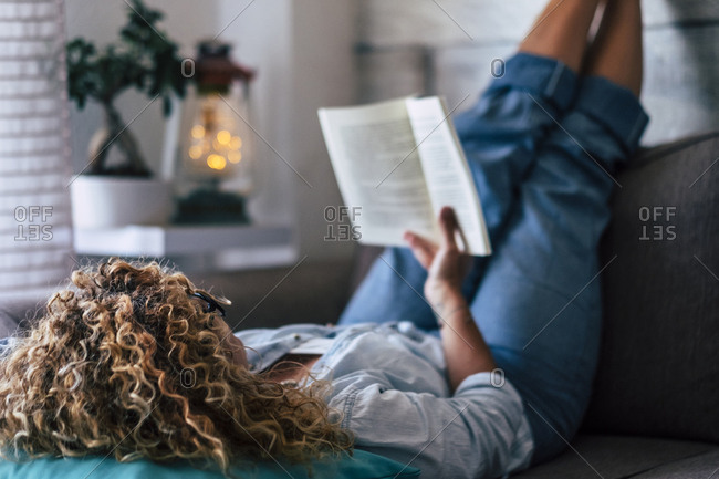 Woman lying on couch at home reading a book