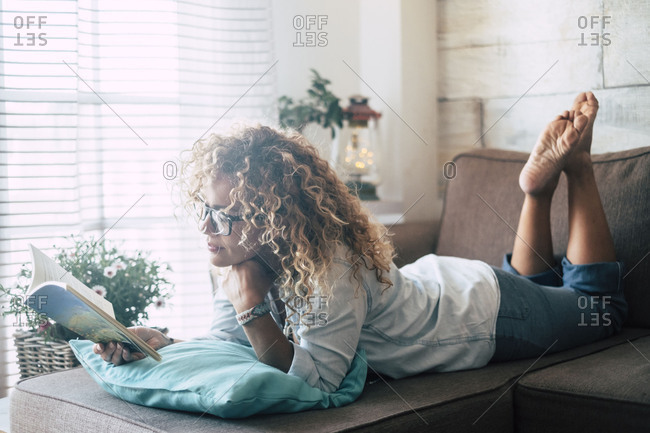 Woman lying on couch at home reading a book