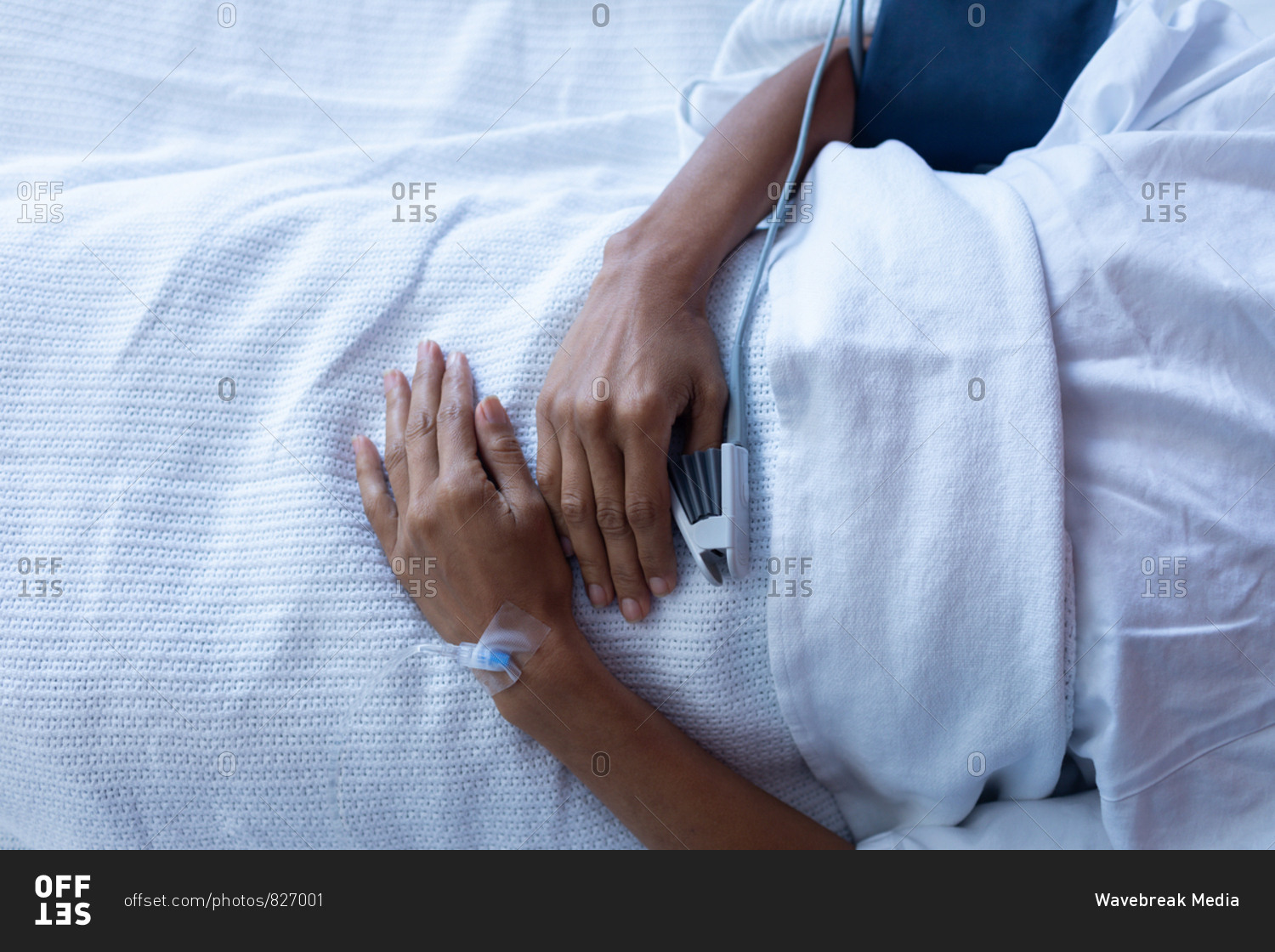 Mid section of mixed-race female patient lying on bed in the ward at hospital. She is getting IV therapy and pulse oximetry is measuring her blood.