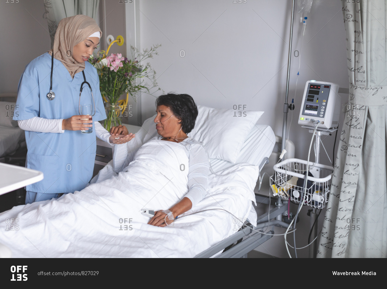 Front view of beautiful mixed-race female doctor in hijab giving medicine to mixed-race female patient in the ward at hospital.