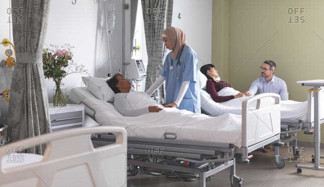 Front view of mixed-race female nurse interacting with mixed-race female patient while diverse couple are next to them in the ward at hospital.