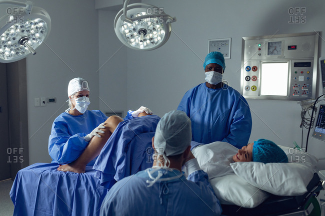 Side view of diverse surgeons examining pregnant Caucasian woman during delivery while Caucasian man holding her hand in operating room at hospital