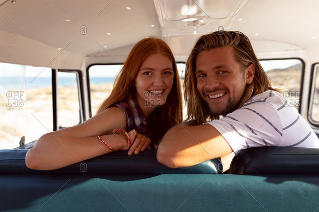 Portrait of happy young Caucasian couple looking at camera in front seat of camper van at beach