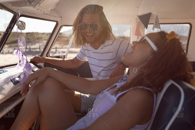 Side view of happy young Diverse couple having fun in front seat of van at beach