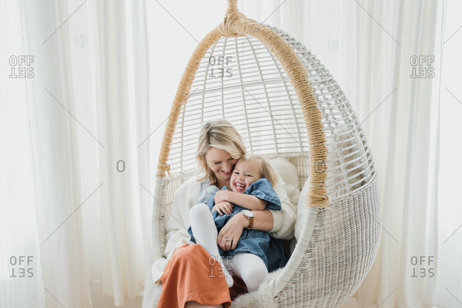 Blonde mom and blonde toddler daughter cuddling in a hanging chair