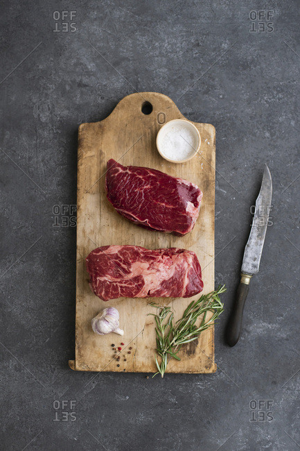 Raw black angus prime beef steak variety on vintage cutting board with rosemary, sea salt and spices