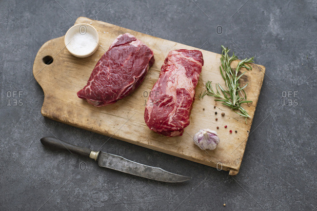 Raw black angus prime beef steak variety on vintage cutting board with rosemary, sea salt and spices