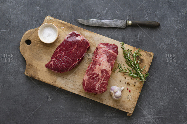 Raw black angus prime beef steak variety on vintage cutting board with rosemary, sea salt and spices
