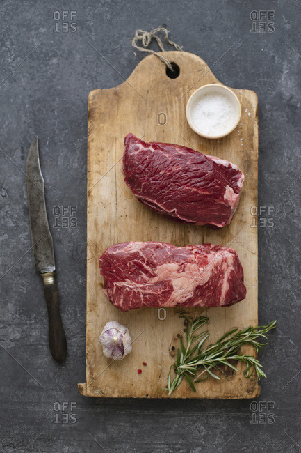 Raw black angus prime beef steak variety on vintage cutting board with rosemary, sea salt and spices