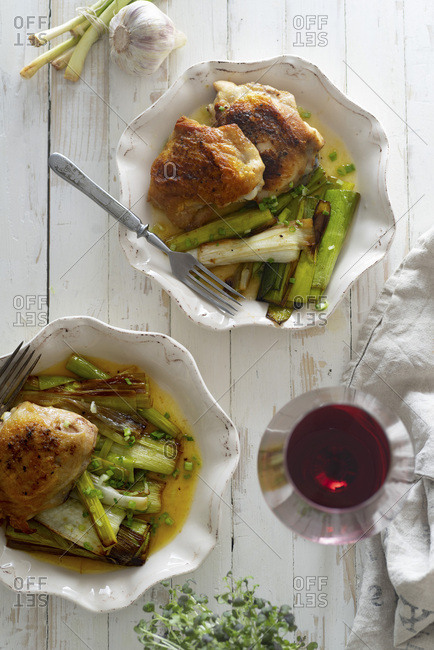 Roasted skin-on chicken thighs with leek and wine sauce on white distressed wooden table