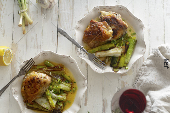 Roasted skin-on chicken thighs with leek and wine sauce on white distressed wooden table