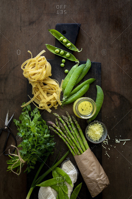 Tagliatelle, vegetables and herbs for home-made Pasta Primavera on black wooden board over wooden background with copy space