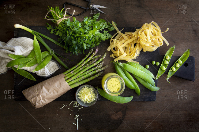 Tagliatelle, vegetables and herbs for home-made Pasta Primavera on black wooden board over wooden background