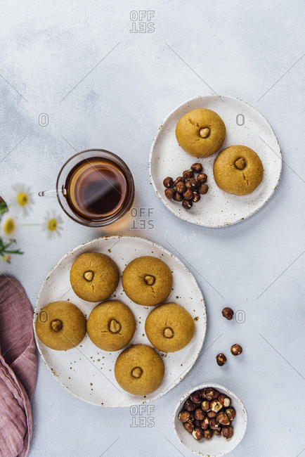 Semolina cookies soaked with sweet syrup on two ceramic plates accompanied by a cup of Turkish tea and hazelnuts