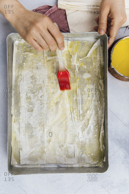 Woman spreading melted butter on baklava phyllo sheets with a brush in a baking sheet