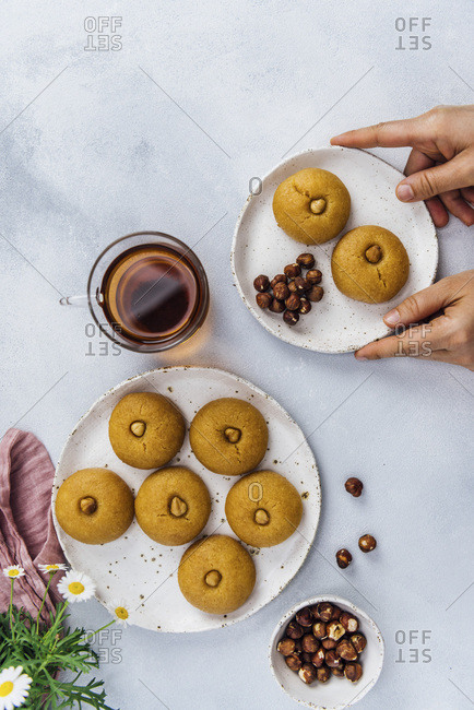 Woman serving semolina cookies soaked with sweet syrup on ceramic plates accompanied by a cup of Turkish tea and hazelnuts