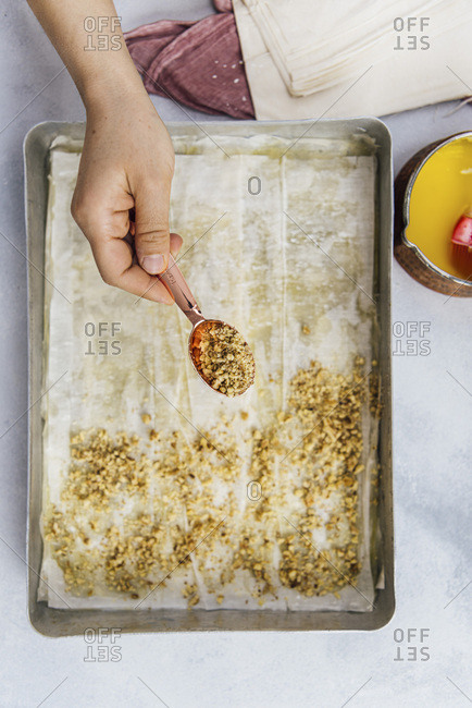 Woman sprinkling crumbled walnuts on phyllo sheets to make Turkish baklava