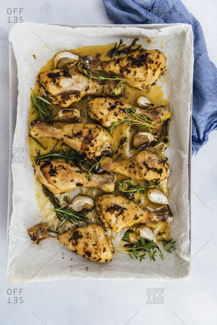 Oven baked chicken legs with herbs and garlic in a baking sheet photographed from top view.