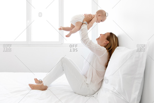 Mother sitting on bed lifting her baby in the air