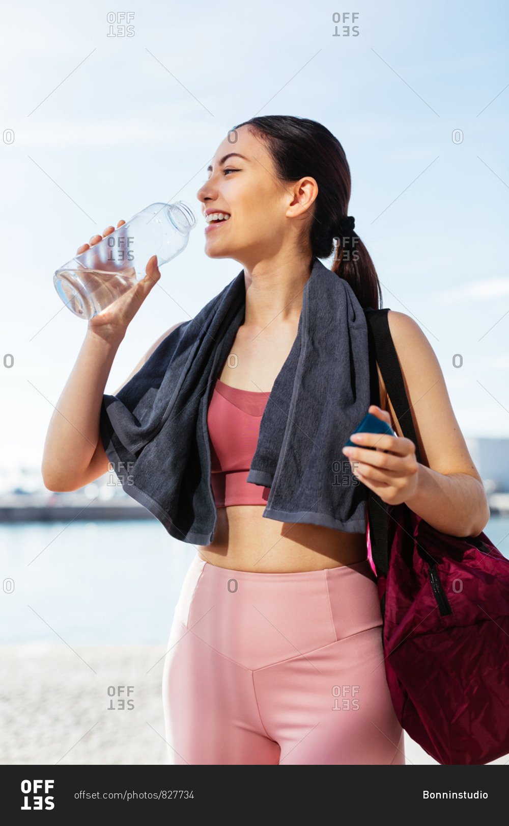 Young woman drinking water wearing sports clothes next to the water