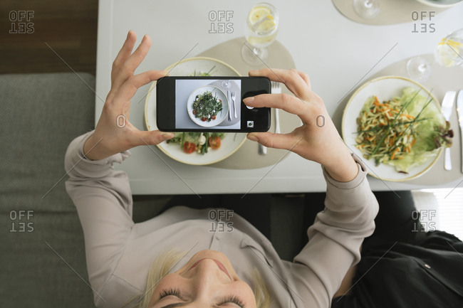 Young woman taking a cell phone picture of a salad in a restaurant