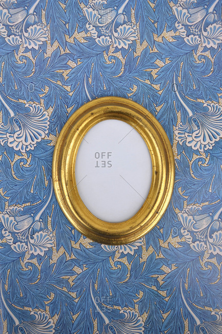 Oval golden picture frame on wallpaper with Art Nouveau floral design
