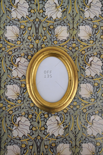 Oval golden picture frame on wallpaper with Art Nouveau floral design