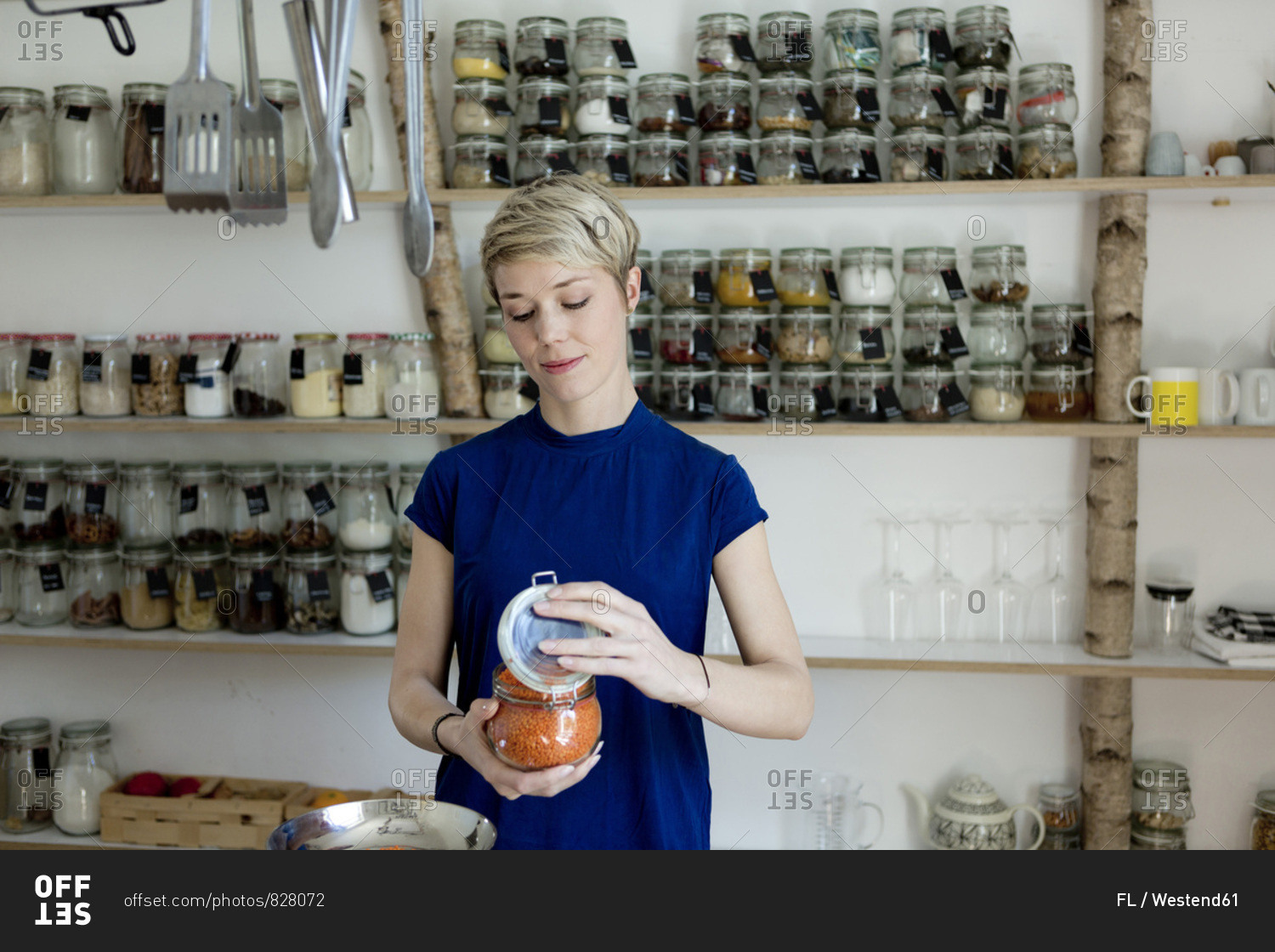 Woman opening jar in front of spice shelf in kitchen