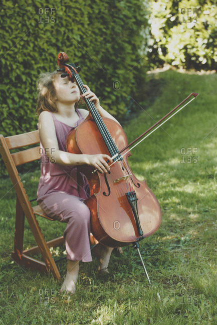 A girl playing the cello  with eyes closed in garden