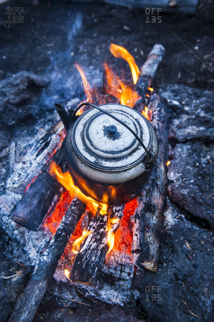 Metal tea kettle heating up over a campfire stock photo - OFFSET