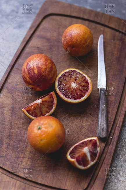 Whole and sliced blood oranges and a kitchen knife on wooden board
