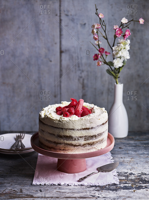 Rhubarb and raspberry sponge cake on a pink cake stand with flowers in background