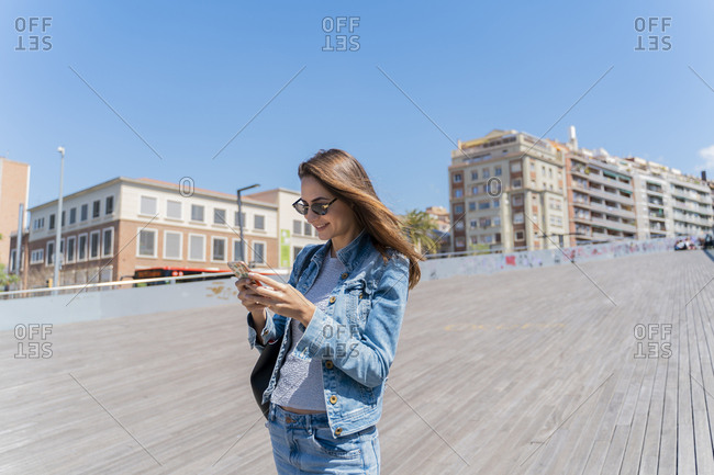 Young woman using smartphone on pedestrian bridge in Barcelona