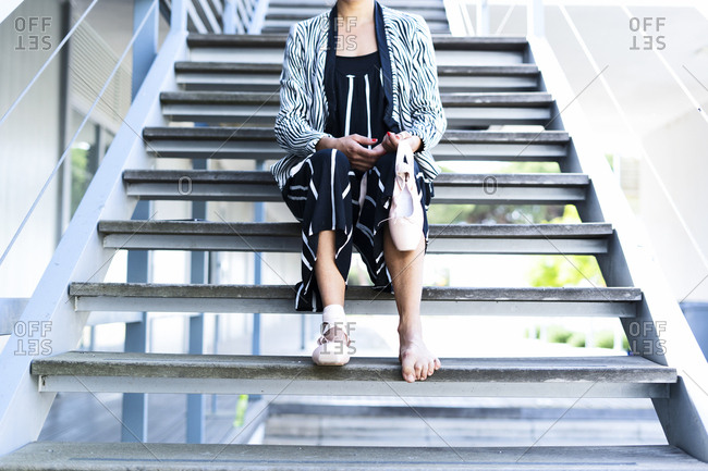 Female dancer with ballet shoes sitting on steps- neck down