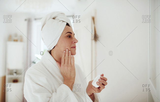Mature woman in a bathroom at home applying moisturizer