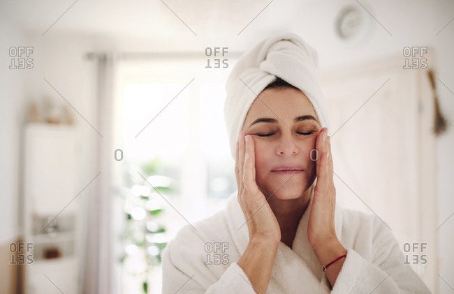Portrait of mature woman in a bathroom at home applying moisturizer