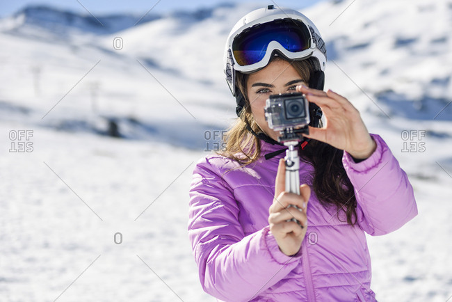 Woman in ski clothes filming with an action camera in snow covered-landscape