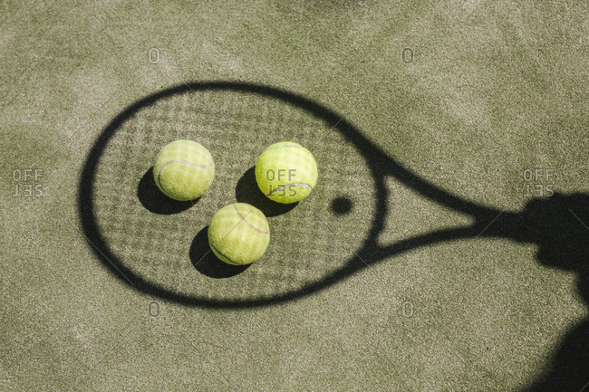 Shadow of a tennis player with balls and racket on court