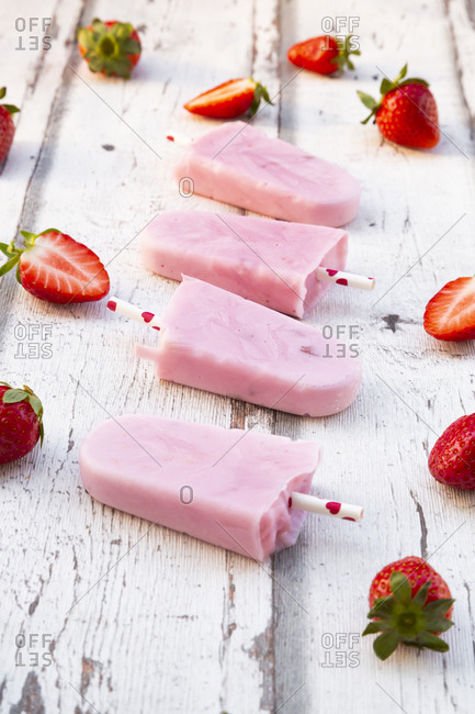 Homemade strawberry yogurt ice lollies with fresh strawberries on white wood