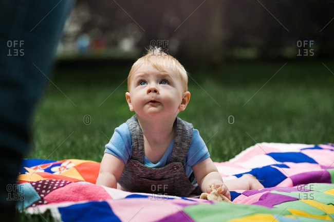 Baby boy on quilt looking up while at a picnic