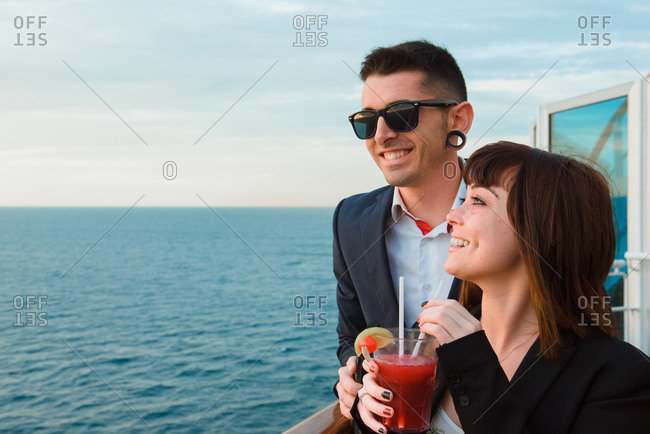 Side view of young attractive couple drinking red beverage with straws from one glass on background of sunset sea