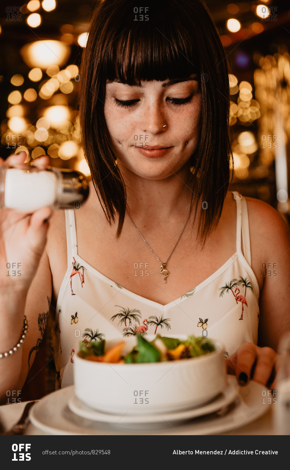 Young lady spilling salt into bowl with yummy vegetable salad while having dinner in luxury restaurant